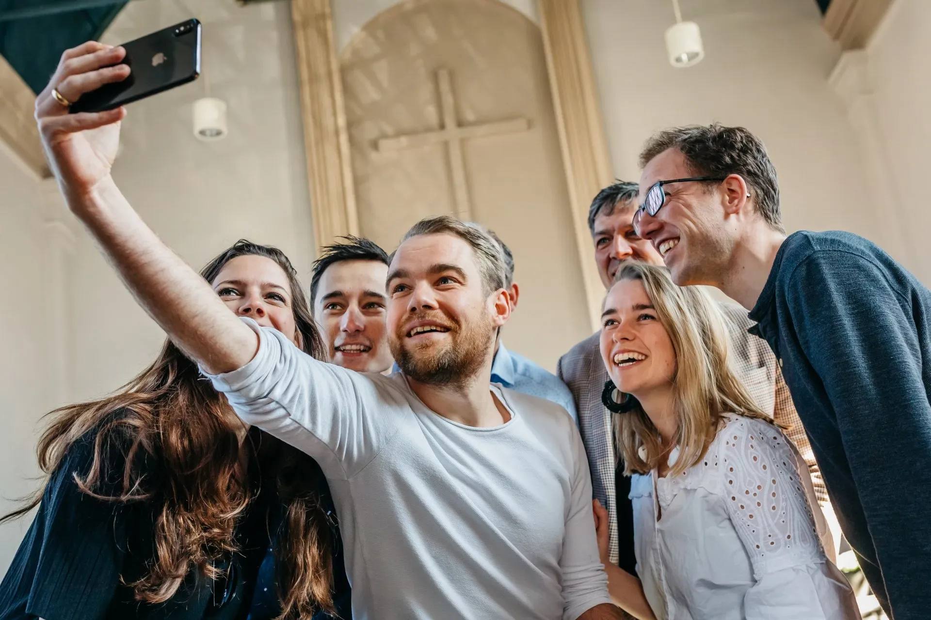 Een groep mensen dicht bij elkaar voor een selfie, lachend, in een hoog en licht kerkinterieur.