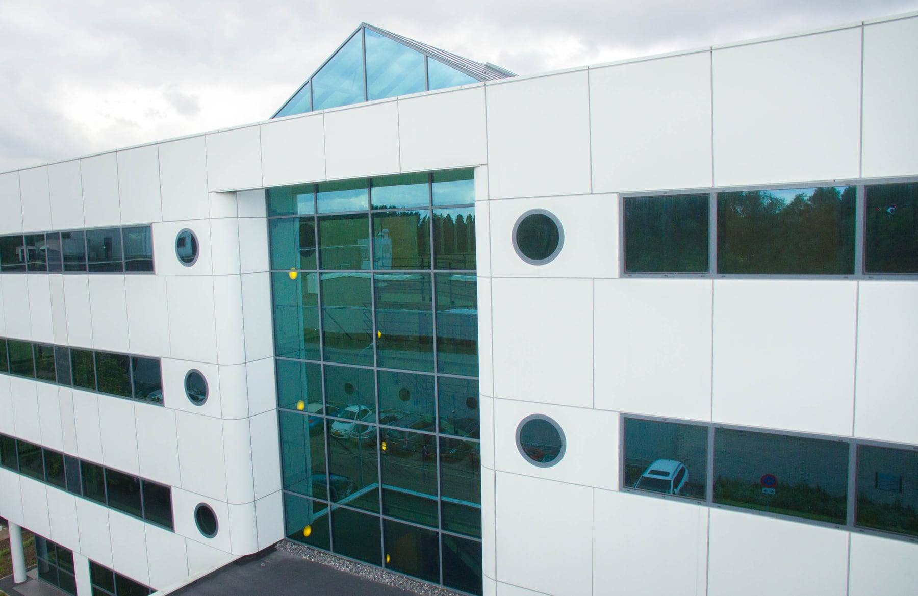 The Fleminglaan 12 office building in Rijswijk from above, filling the frame: white panelled elevation, round windows, and a full-height glazed atrium under a pitched glass roof.